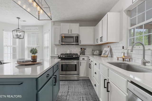 kitchen featuring light countertops, white cabinets, a sink, a notable chandelier, and stainless steel appliances