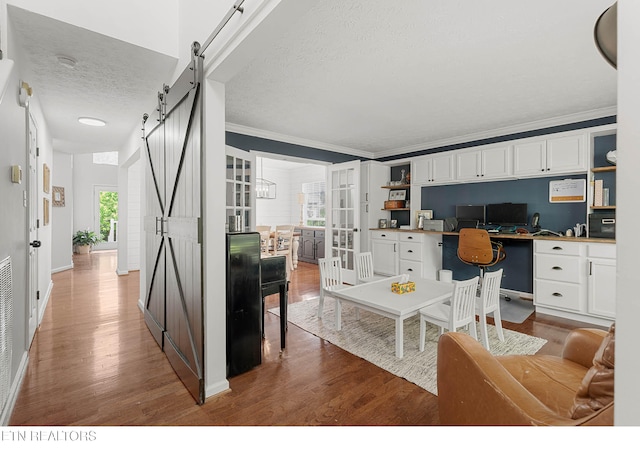 living room featuring a barn door, built in study area, a textured ceiling, wood finished floors, and ornamental molding