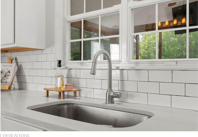 room details with a sink, light countertops, white cabinets, and decorative backsplash