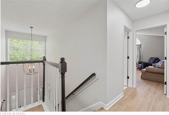 corridor featuring baseboards, a textured ceiling, light wood finished floors, and an upstairs landing