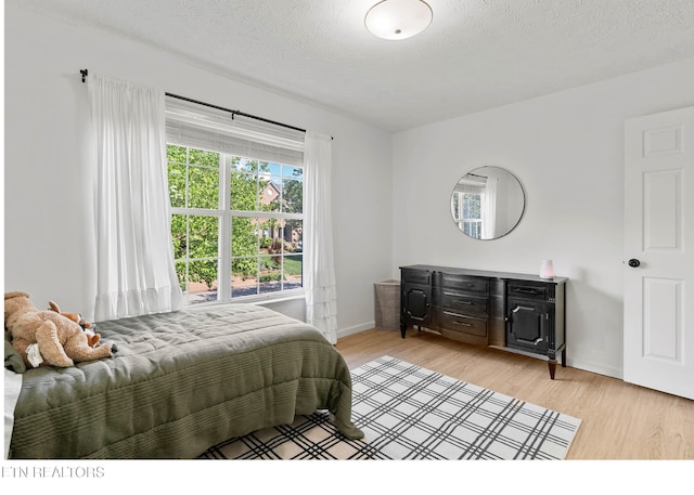 bedroom with baseboards, light wood-type flooring, and a textured ceiling