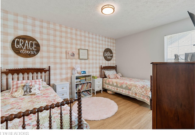 bedroom featuring a textured ceiling, wood finished floors, and wallpapered walls