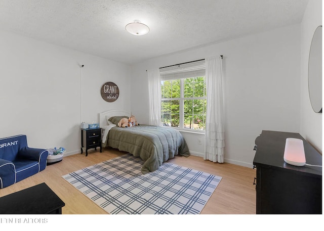 bedroom featuring baseboards, a textured ceiling, and wood finished floors