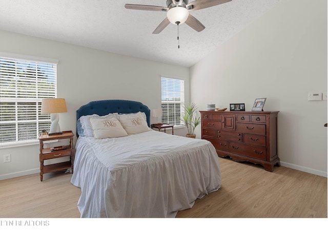 bedroom featuring ceiling fan, a textured ceiling, baseboards, lofted ceiling, and light wood-style floors