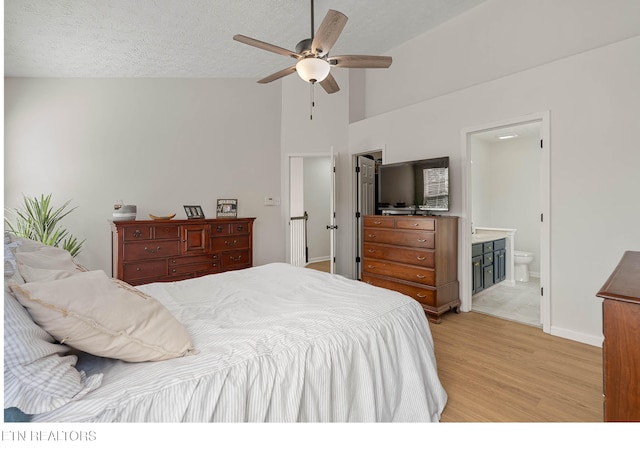bedroom featuring ceiling fan, light wood finished floors, ensuite bath, high vaulted ceiling, and baseboards