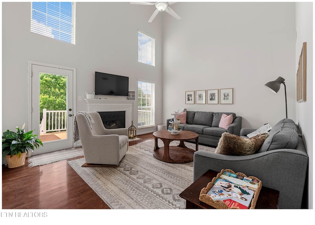 living room featuring a fireplace with flush hearth, a ceiling fan, wood finished floors, and a towering ceiling