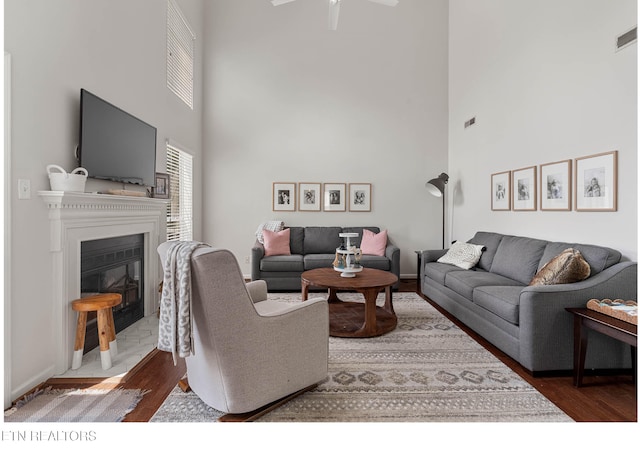 living room featuring a fireplace with flush hearth, ceiling fan, wood finished floors, and a towering ceiling