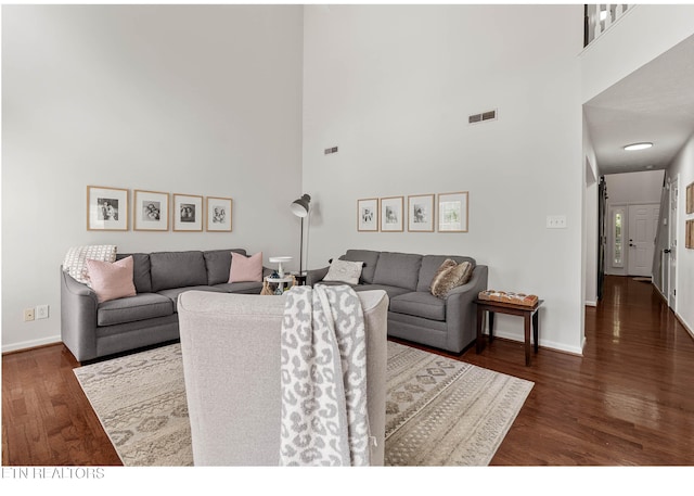 living room featuring visible vents, baseboards, a towering ceiling, and wood finished floors