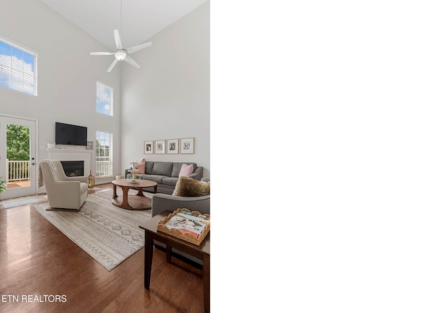 living room featuring a glass covered fireplace, a high ceiling, a ceiling fan, and wood finished floors