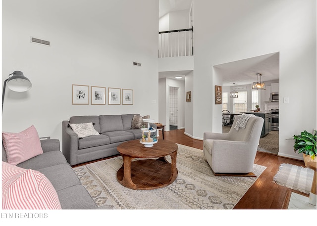 living room featuring baseboards, a high ceiling, visible vents, and wood finished floors