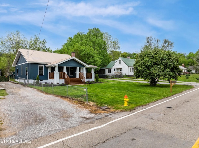 bungalow-style home with covered porch, metal roof, a fenced front yard, gravel driveway, and a front lawn