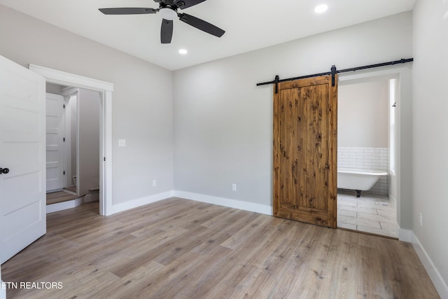 unfurnished bedroom with baseboards, light wood-type flooring, recessed lighting, a barn door, and connected bathroom