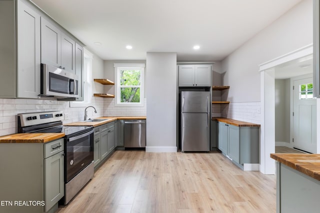 kitchen featuring gray cabinetry, open shelves, appliances with stainless steel finishes, and wooden counters