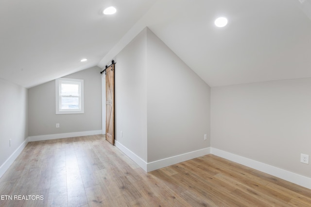 additional living space featuring light wood-style floors, a barn door, lofted ceiling, and recessed lighting