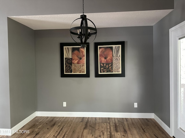 spare room with a textured ceiling, baseboards, a notable chandelier, and dark wood finished floors