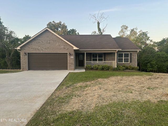 single story home featuring brick siding, a garage, covered porch, and a front yard