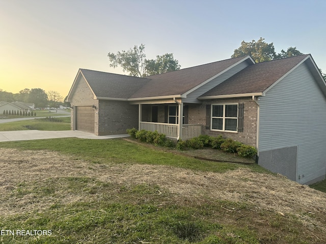 exterior space featuring brick siding, concrete driveway, an attached garage, a yard, and a porch