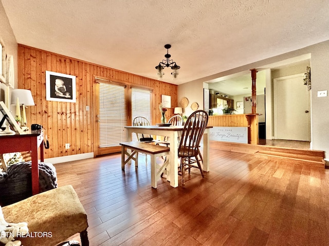 dining space featuring a textured ceiling, wood walls, baseboards, an inviting chandelier, and hardwood / wood-style floors