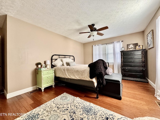 bedroom with baseboards, ceiling fan, a textured ceiling, and wood finished floors