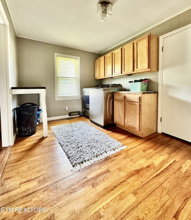 clothes washing area featuring ornamental molding, cabinet space, light wood-type flooring, and washer / clothes dryer