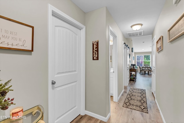 hallway with visible vents, light wood-style floors, and baseboards