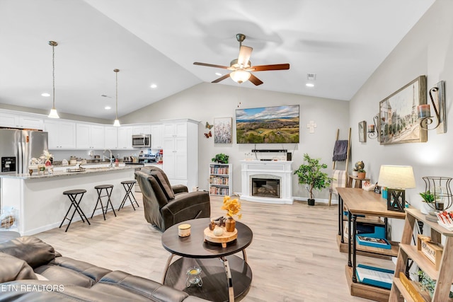 living room featuring light wood-style floors, a glass covered fireplace, a ceiling fan, recessed lighting, and lofted ceiling