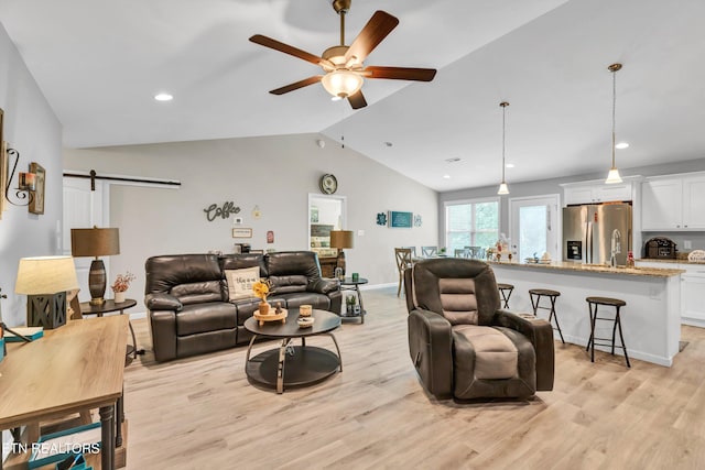 living area with a barn door, a ceiling fan, recessed lighting, lofted ceiling, and light wood-type flooring