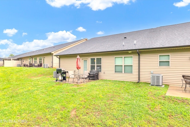 rear view of house featuring central air condition unit, a patio, a shingled roof, and a yard