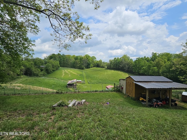 view of yard featuring an outdoor structure, a pole building, fence, and a rural view