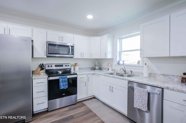 kitchen with crown molding, white cabinets, a sink, stainless steel appliances, and wood finished floors