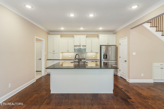 kitchen with stainless steel fridge, under cabinet range hood, a center island with sink, and dark countertops