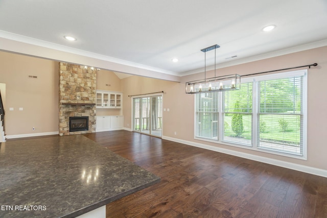 unfurnished living room with crown molding, plenty of natural light, a stone fireplace, and dark wood-type flooring