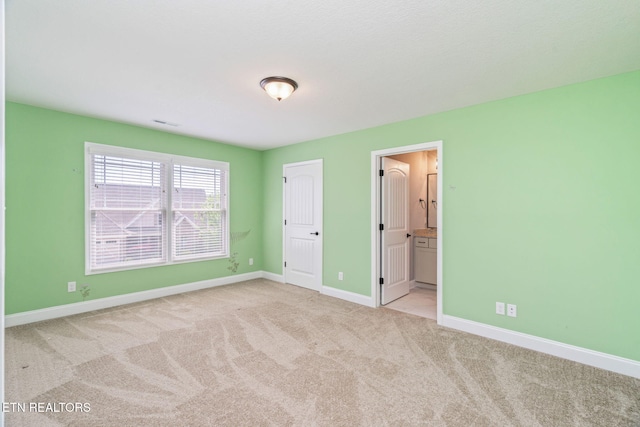unfurnished bedroom with baseboards, light carpet, and ensuite bath