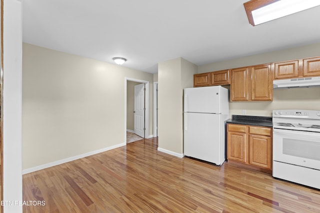 kitchen featuring dark countertops, baseboards, light wood-style floors, under cabinet range hood, and white appliances