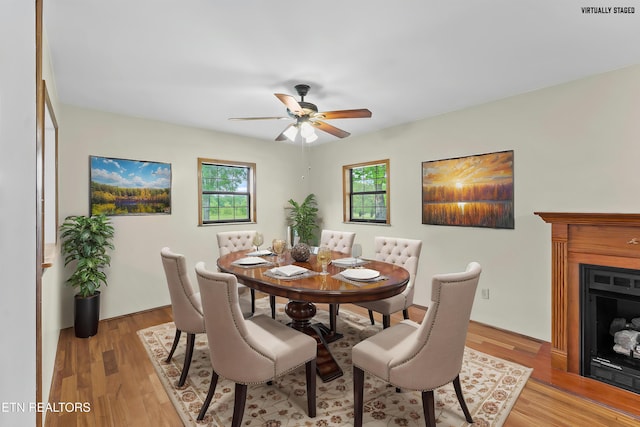dining room with ceiling fan, a fireplace, and light wood-type flooring