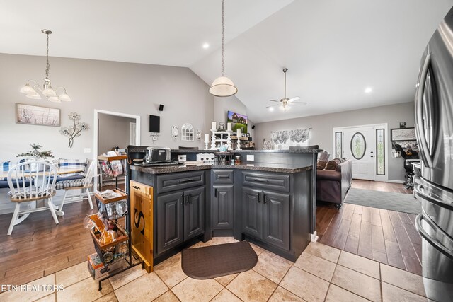 kitchen with pendant lighting, ceiling fan with notable chandelier, vaulted ceiling, and dark countertops