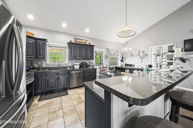 kitchen with a breakfast bar area, decorative light fixtures, dark countertops, a sink, and stainless steel appliances