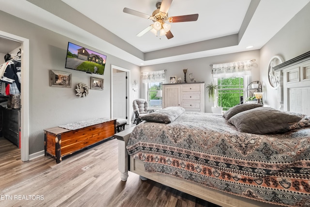 bedroom with a ceiling fan, wood finished floors, baseboards, a closet, and a spacious closet