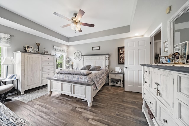 bedroom with dark wood-type flooring, ceiling fan, and a tray ceiling