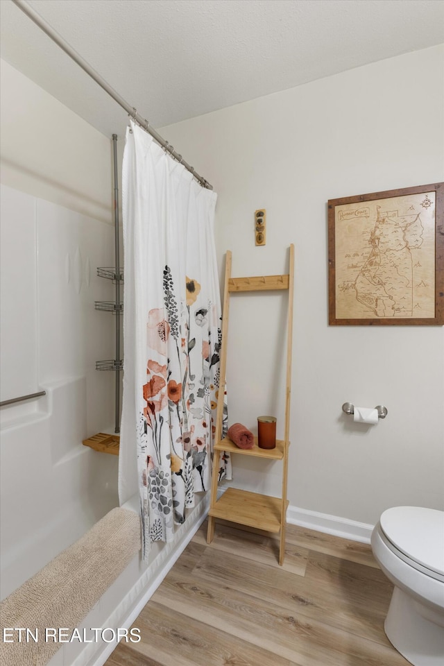 full bath featuring baseboards, toilet, a shower with curtain, and wood finished floors