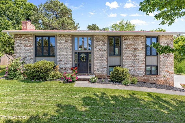view of front of house featuring a chimney, a front lawn, and brick siding