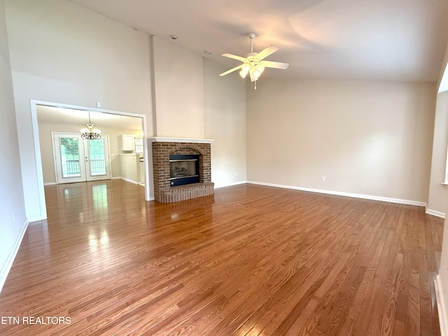 unfurnished living room featuring baseboards, wood finished floors, ceiling fan with notable chandelier, and high vaulted ceiling