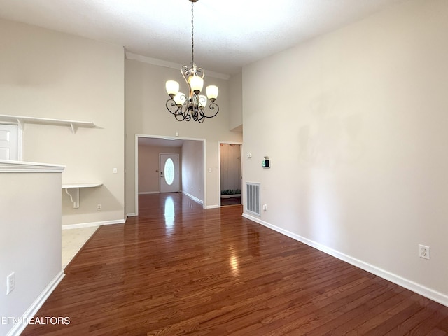 unfurnished dining area with an inviting chandelier, wood finished floors, visible vents, baseboards, and a towering ceiling