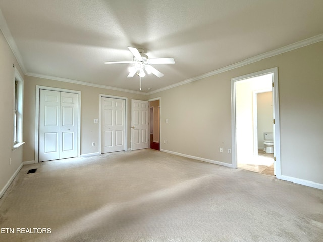 unfurnished bedroom with light colored carpet, ornamental molding, multiple closets, visible vents, and baseboards
