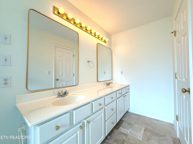 bathroom with baseboards, stone finish flooring, double vanity, and a sink