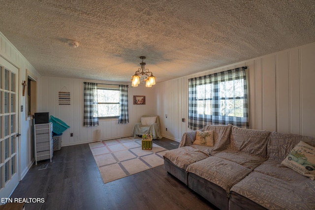 living area featuring a decorative wall, wood finished floors, baseboards, a textured ceiling, and a chandelier