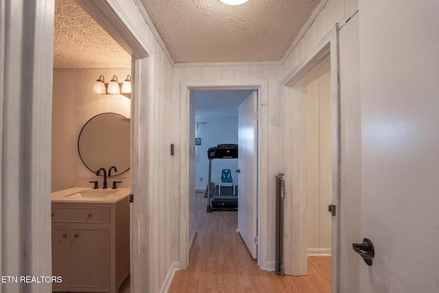 hall with a sink, baseboards, light wood finished floors, and a textured ceiling