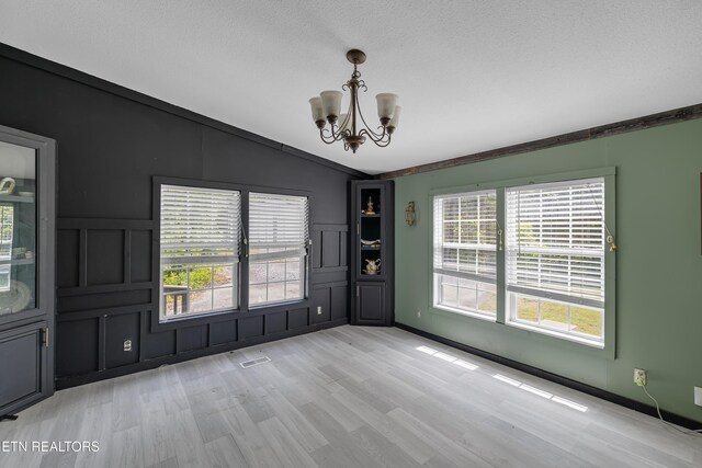 spare room featuring lofted ceiling, a wainscoted wall, a notable chandelier, light wood-style floors, and a decorative wall