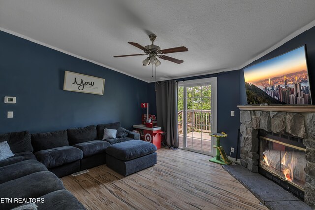 living area featuring ceiling fan, a textured ceiling, a fireplace, wood finished floors, and ornamental molding