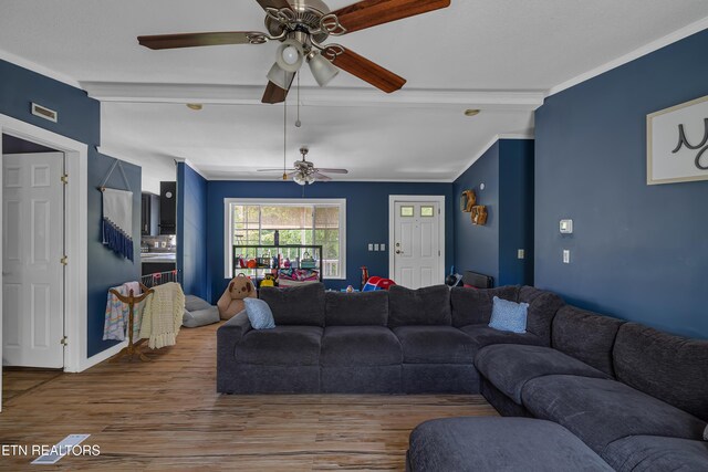 living area with crown molding, ceiling fan, wood finished floors, and beam ceiling